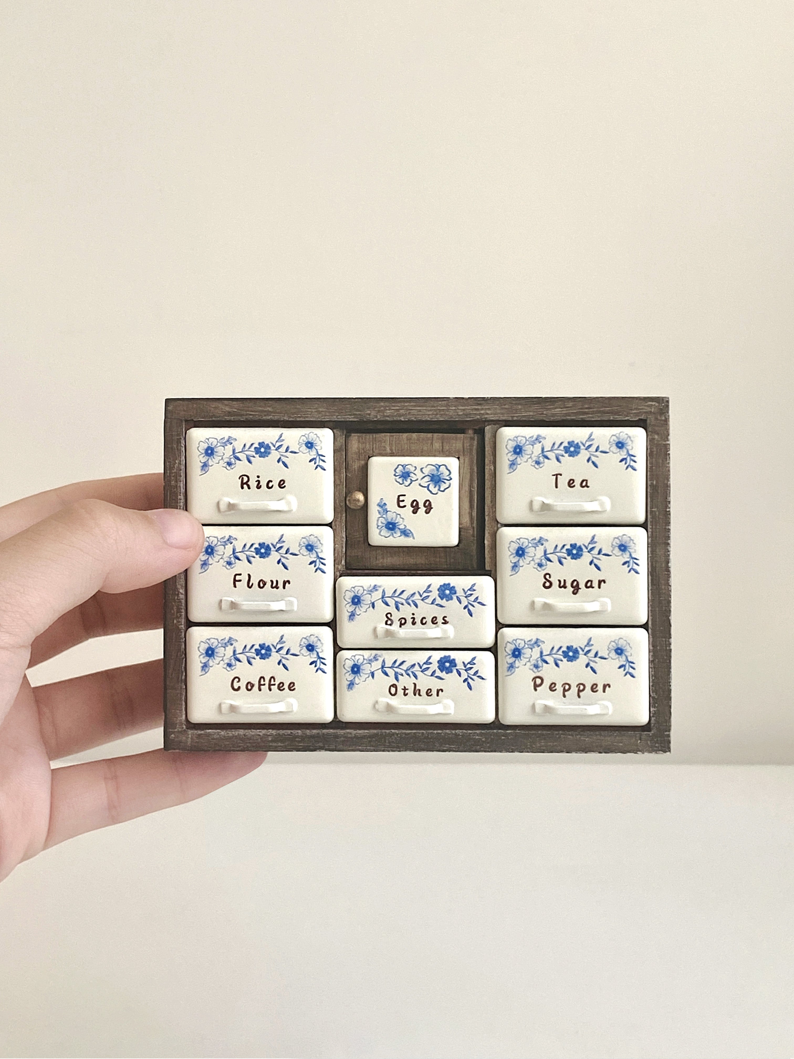 Antler Brown miniature spice cabinet held in hand with cream blue floral pantry drawers